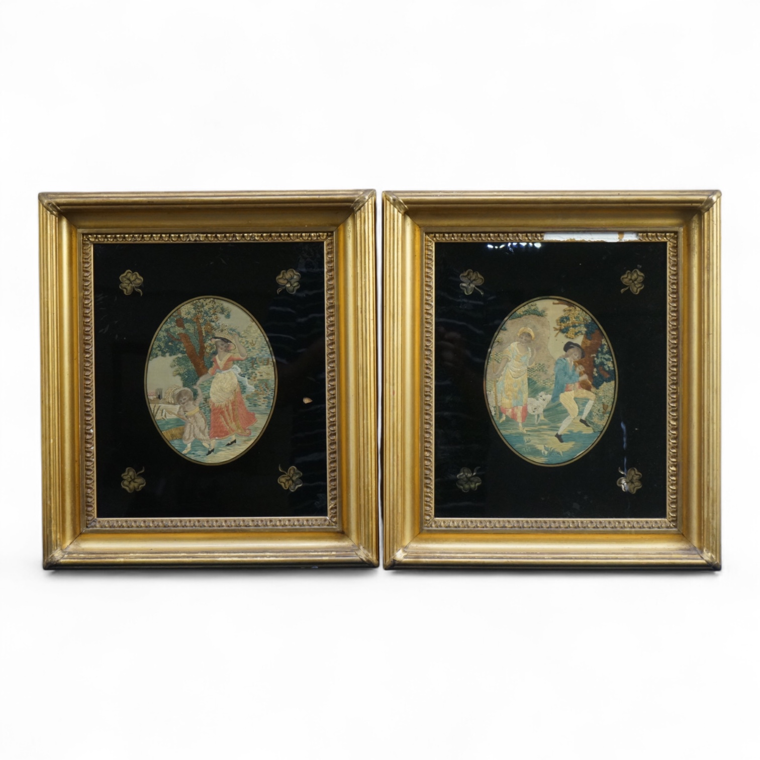 Two early 19th century oval silk worked embroideries. Both figural pastoral scenes, mostly worked in stem stitch, the leaves in a stump work style knotting. Both embroideries set within decorative Verre Eglomise glass an